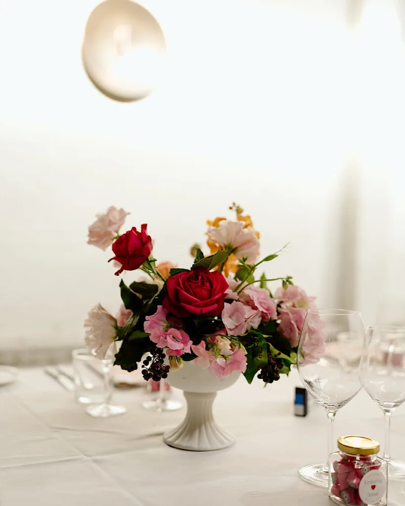 Reception centrepiece of red and blush roses in a white footed bowl on a set table