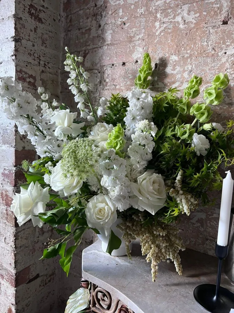 White-and-green pedestal arrangement against a raw brick wall on a marble mantel