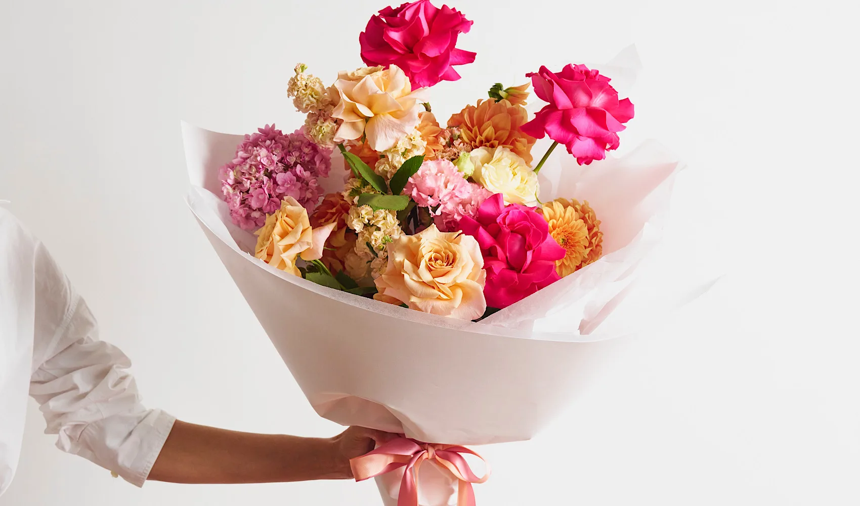 A hand-tied Bloom Republica bouquet of hot-pink and peach roses, pink hydrangea and orange dahlias, wrapped in blush paper and ribbon