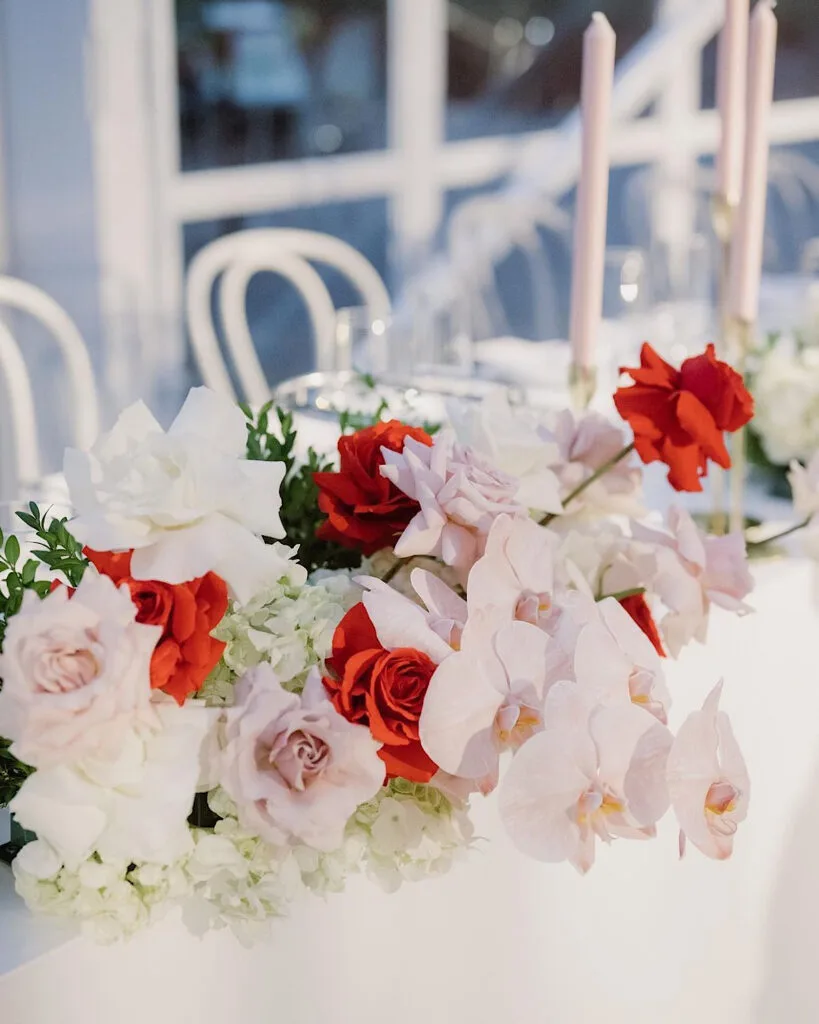 Head-table garland of white hydrangea, blush orchids and red roses with pink taper candles