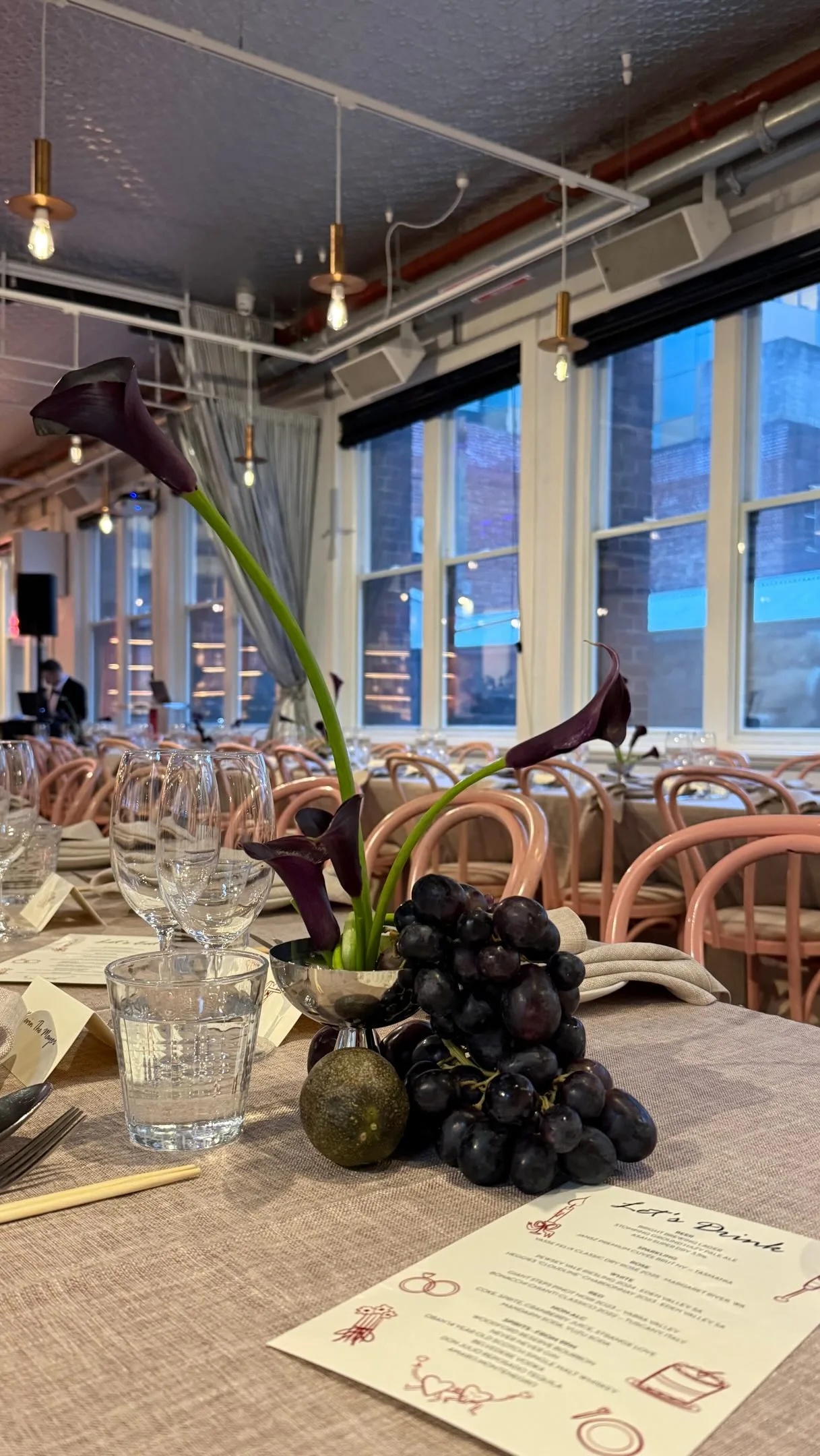 Burgundy calla lilies and black grapes on a linen loft reception table with pink bentwood chairs